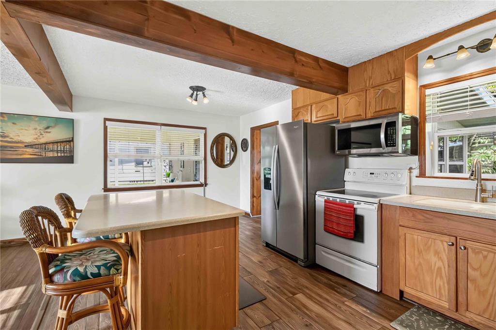A kitchen features wood cabinets, stainless steel appliances, a center island, and a wooden ceiling beam — 4704 PARK ACRES DRIVE, BRADENTON, FL