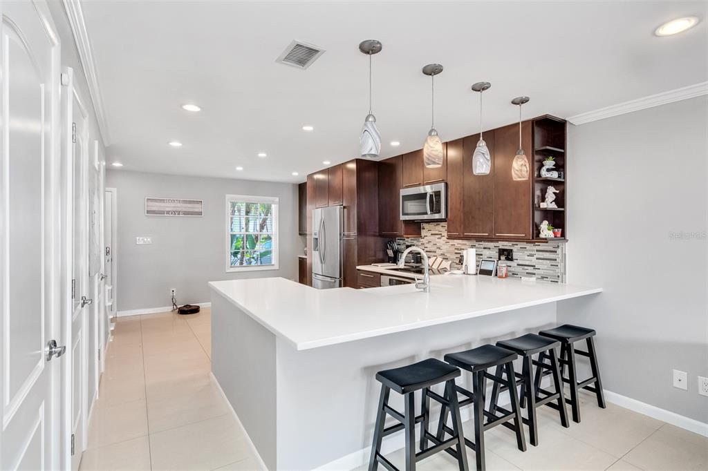 A modern kitchen features dark wood cabinets, white countertops, a breakfast bar, and pendant lighting — 4779 COQUINA KEY DRIVE SE, ST PETERSBURG, FL