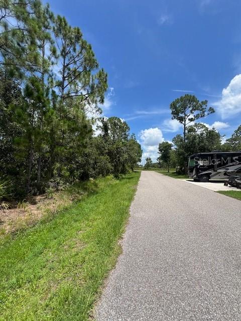 A paved road runs alongside a wooded area with a parked RV in the distance — 23324 AIRWAY AVENUE, PUNTA GORDA, FL