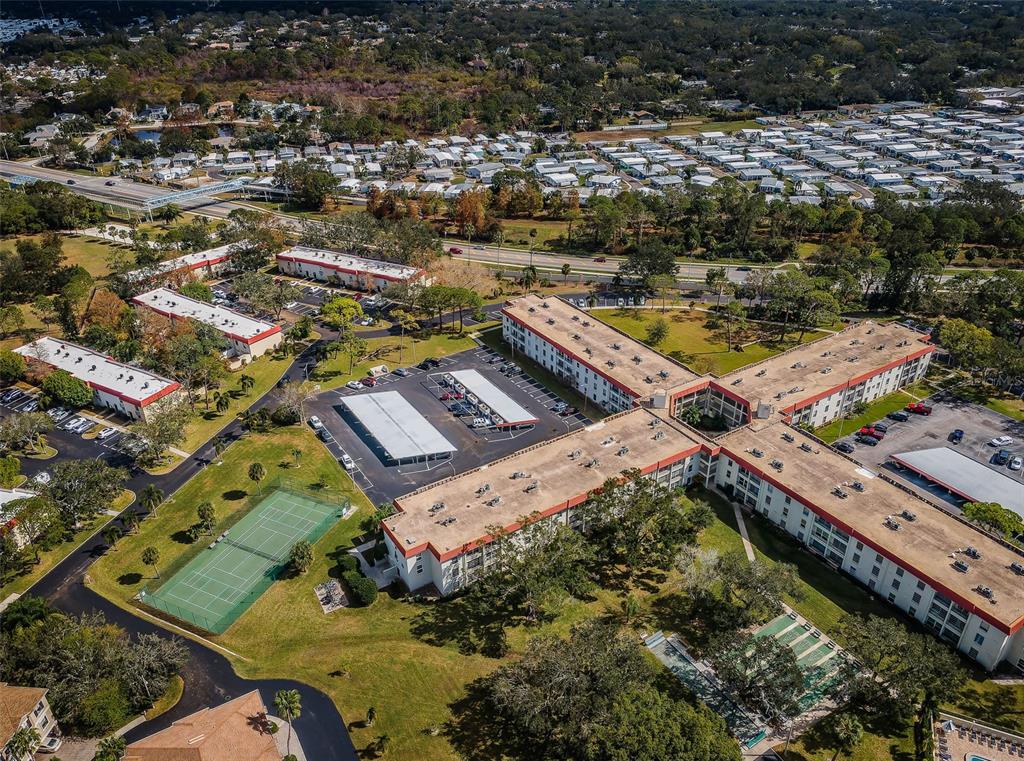 An aerial view shows a multi-story apartment complex with a tennis court and parking lots — 2700 BAYSHORE BOULEVARD UNIT 3208, DUNEDIN, FL