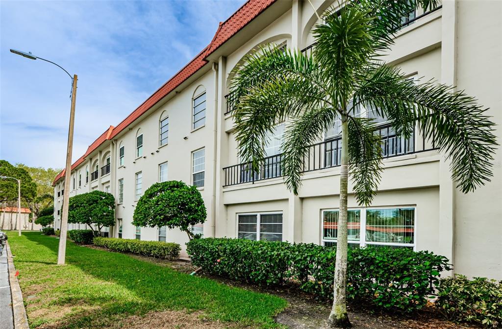 A multi-story apartment building features a palm tree, manicured hedges, and a grassy lawn — 2700 BAYSHORE BOULEVARD UNIT 3208, DUNEDIN, FL