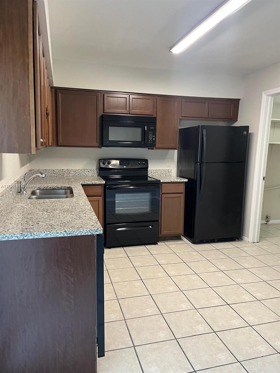 A kitchen features dark wood cabinets, black appliances, granite countertops, and light-colored floor tiles — 4002 Dolomite # A, Orlando FL 32839, ORLANDO, FL