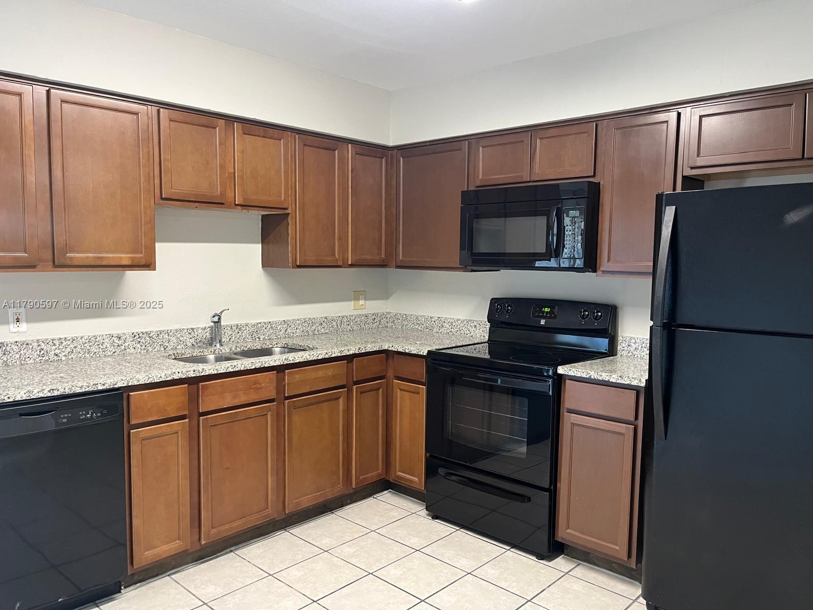 A kitchen features wood cabinets, granite countertops, black appliances, and light-colored tile flooring — 4002 Dolomite # A, Orlando FL 32839, ORLANDO, FL