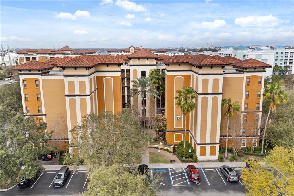 An aerial view shows a multi-story, orange-stucco apartment building with a tile roof and parking — 12539 FLORIDAYS RESORT DRIVE UNIT 404D, ORLANDO, FL