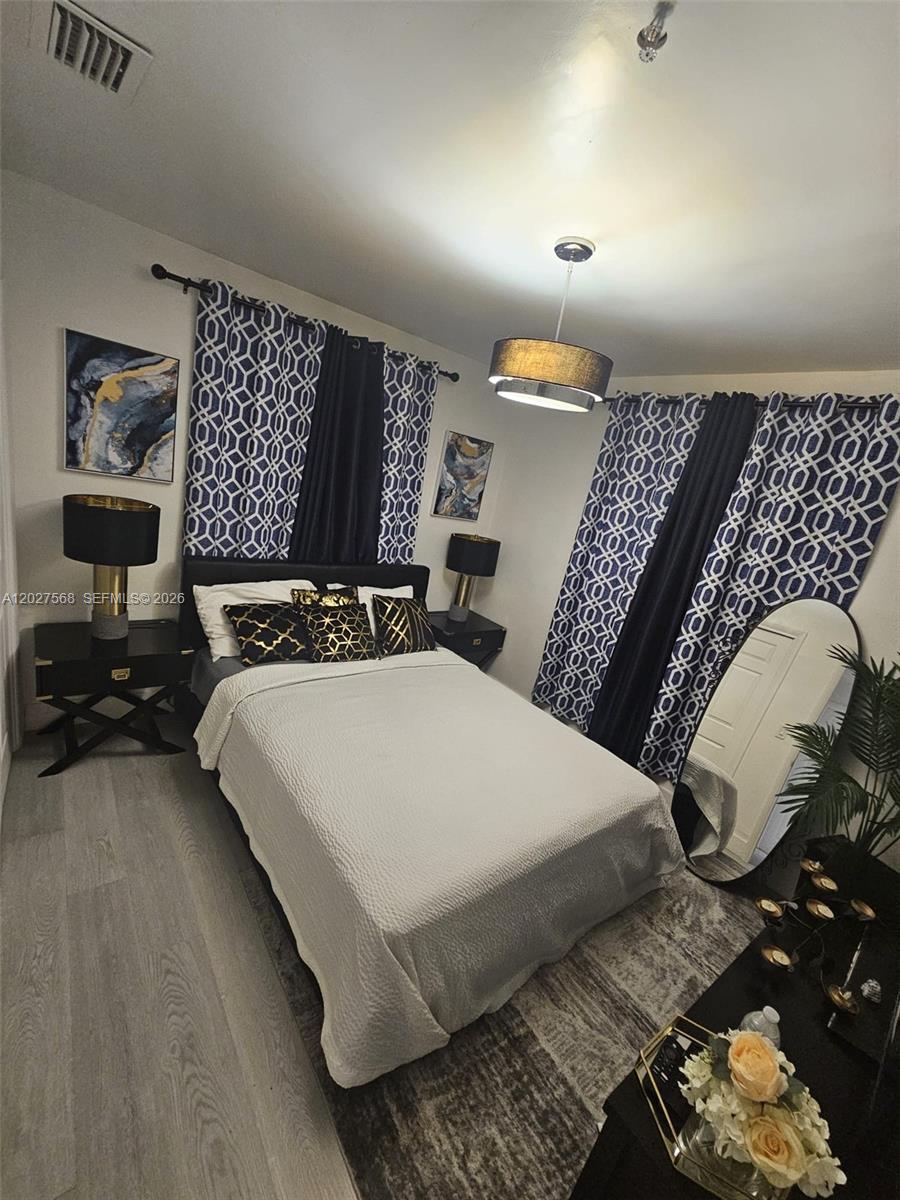 A bedroom features a bed with patterned curtains, gold-accented decor, and light wood-look flooring — 4890 NW 7th St # 2, Plantation FL 33317, PLANTATION, FL