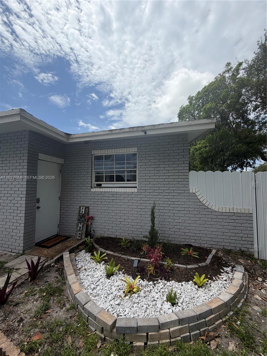 A gray brick house exterior features a curved stone garden bed and a white door — 4890 NW 7th St # 2, Plantation FL 33317, PLANTATION, FL