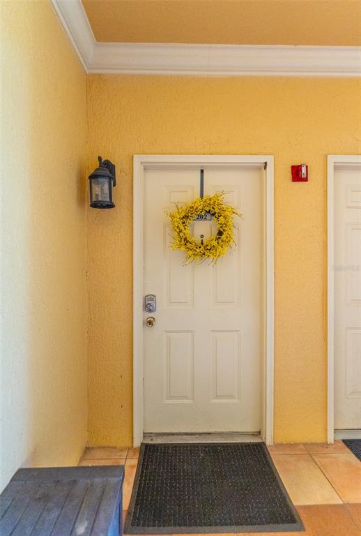 A white front door with a yellow wreath is set in a yellow exterior wall — 4306 BAYSIDE VILLAGE DRIVE UNIT 202, TAMPA, FL