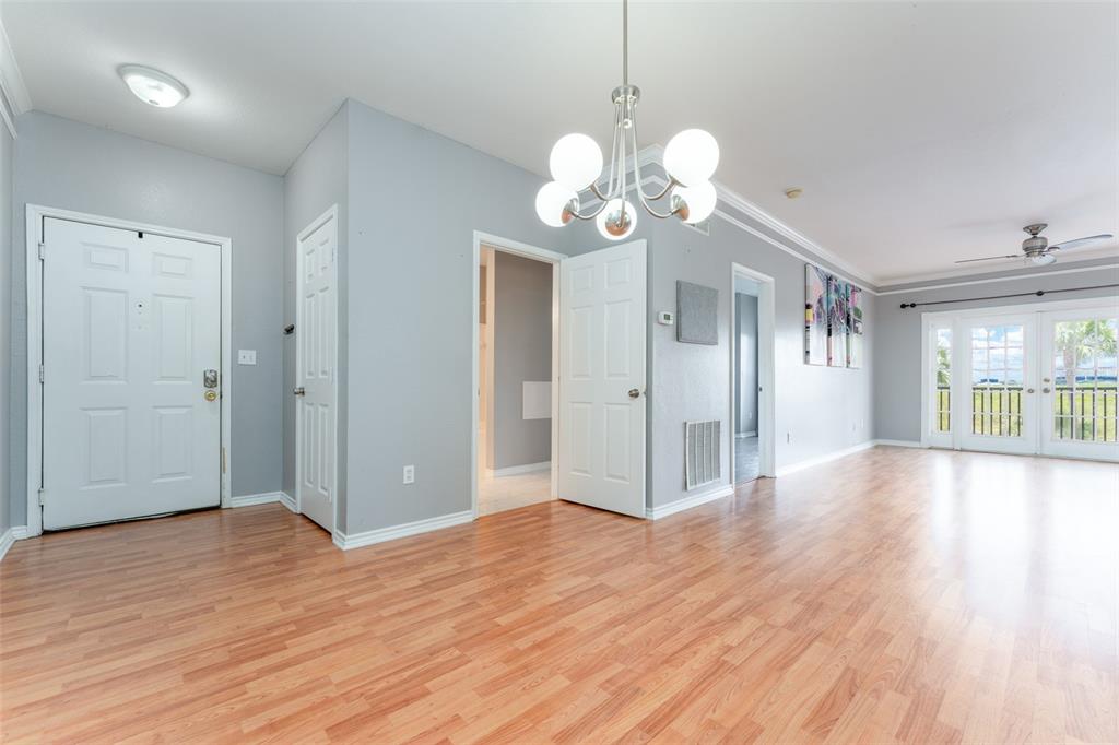 An interior view shows a living area with light wood flooring, gray walls, and a chandelier — 4306 BAYSIDE VILLAGE DRIVE UNIT 202, TAMPA, FL