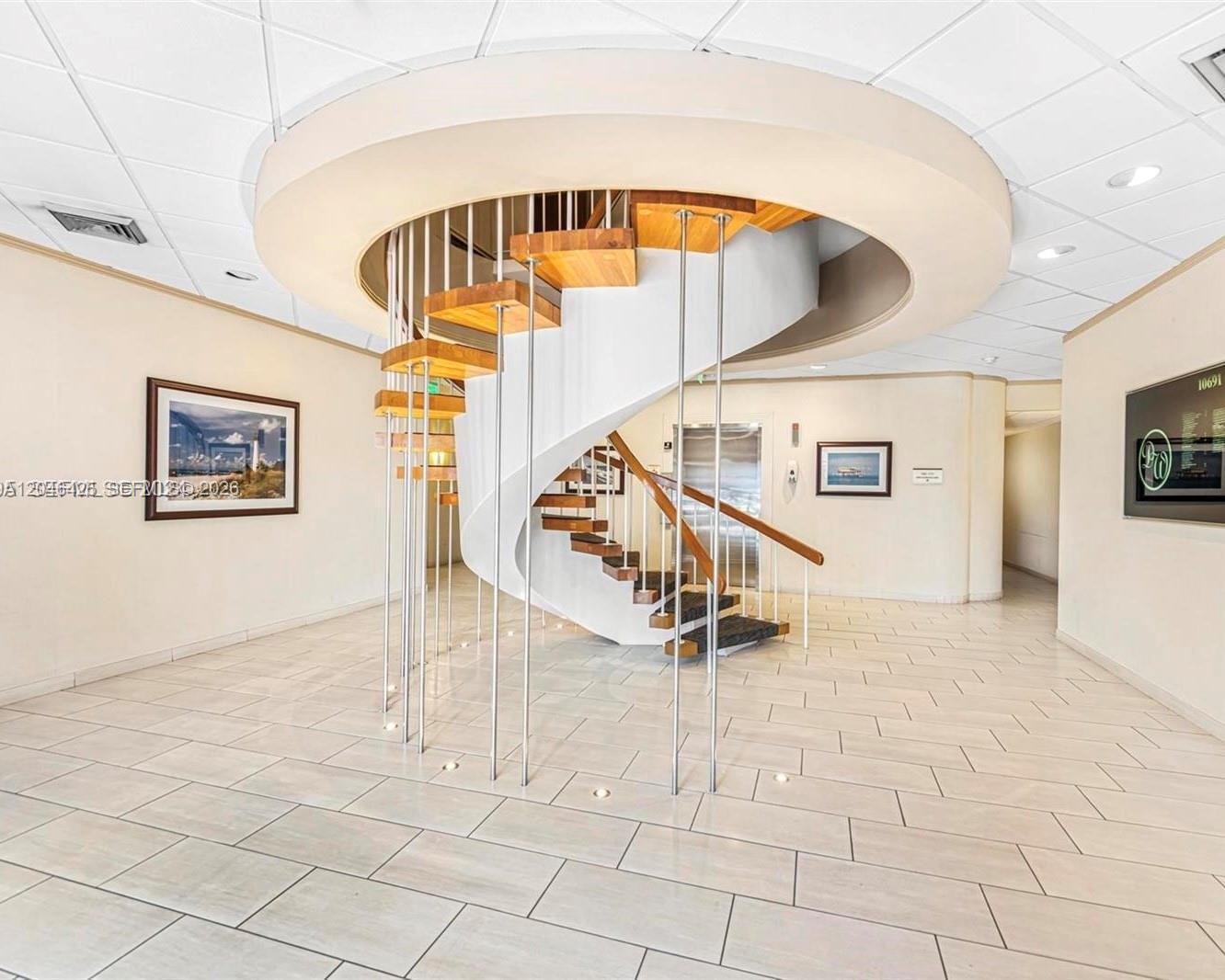 A spiral staircase with wooden treads and metal railings sits in a tiled lobby — 10691 SW 88th St, Miami FL 33176, MIAMI, FL
