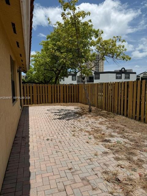 A paved patio area sits beside a wooden fence and a tree in a backyard — MIAMI, FL