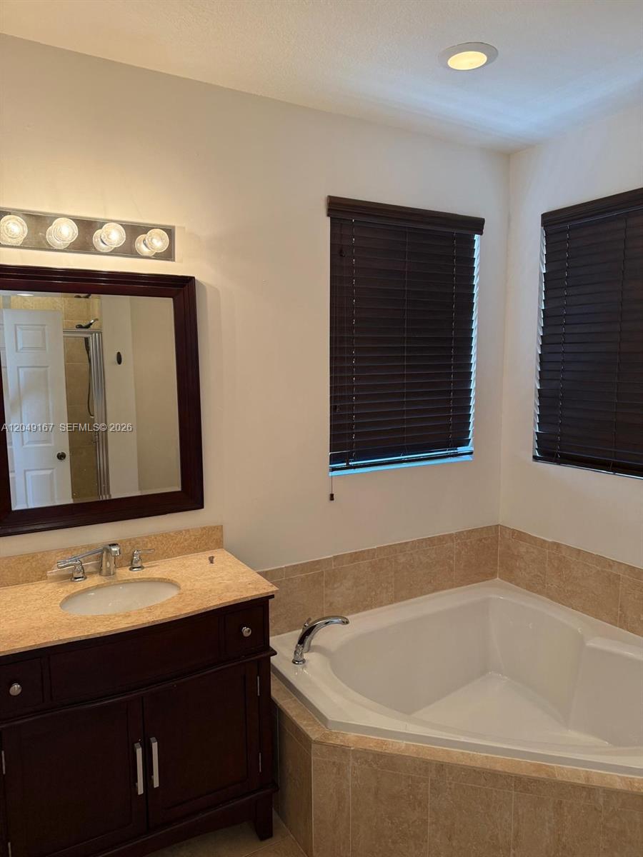 A bathroom features a dark wood vanity, a corner soaking tub, and two windows — MIAMI, FL