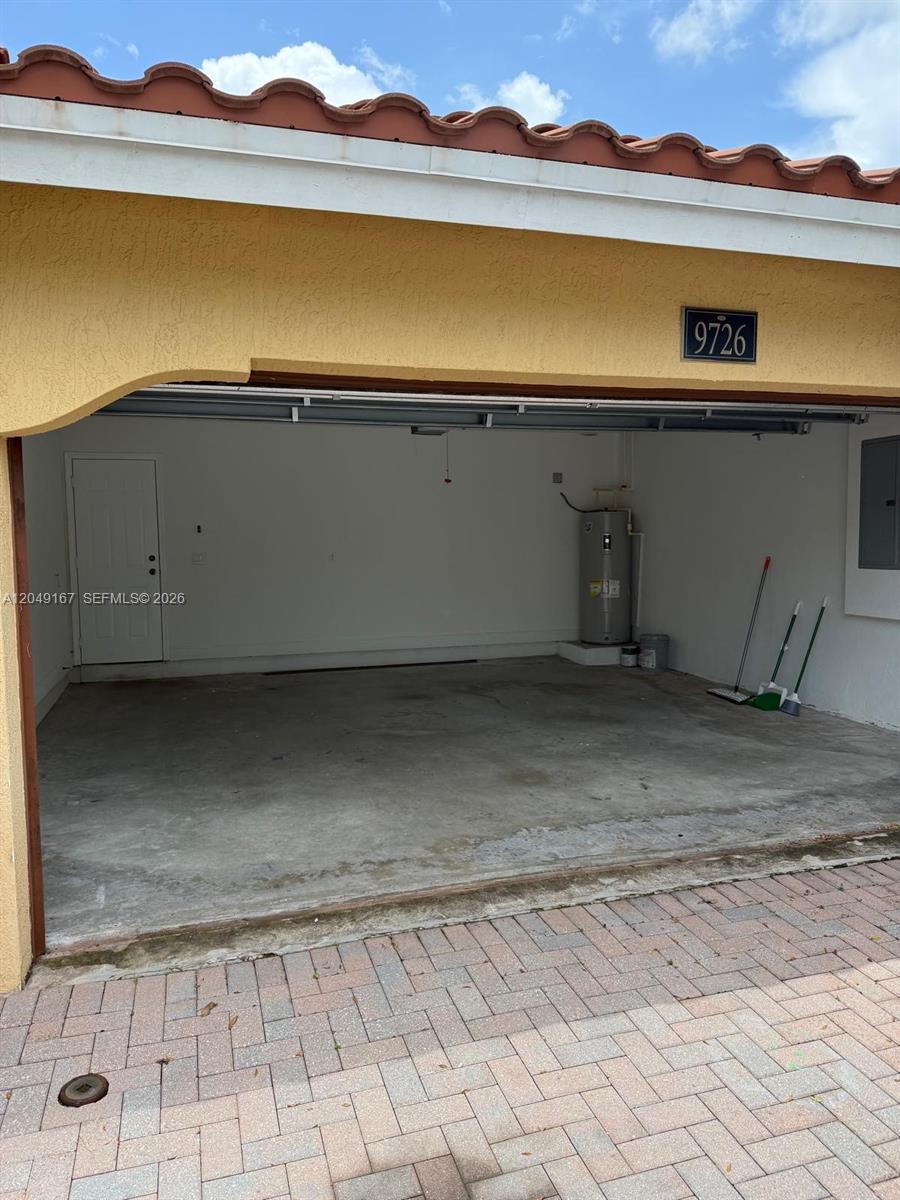 An open garage features a concrete floor, a water heater, and a side entry door — MIAMI, FL