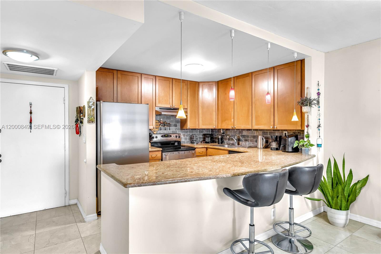 A kitchen features wooden cabinets, a granite breakfast bar, and stainless steel appliances — 600 Three Islands Blvd # 618, Hallandale Beach FL 33009, HALLANDALE BEACH, FL