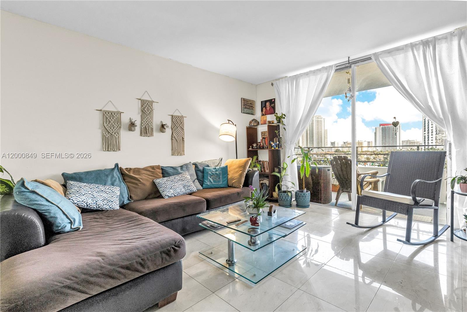 A living room features a brown sectional sofa, glass coffee table, and balcony with city views — 600 Three Islands Blvd # 618, Hallandale Beach FL 33009, HALLANDALE BEACH, FL