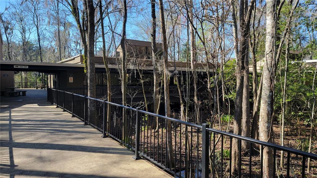 A paved walkway with a black metal railing leads toward a building nestled among trees — 2301 PARK AVENUE UNIT #300, ORANGE PARK, FL