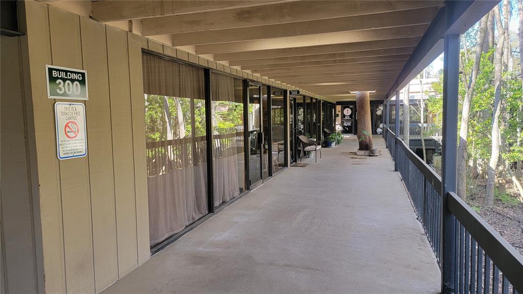 An exterior walkway with a railing leads past glass-fronted office suites in a wooded setting — 2301 PARK AVENUE UNIT #300, ORANGE PARK, FL