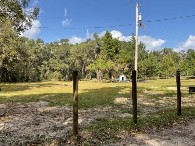 A grassy, partially cleared lot features three wooden fence posts in the foreground — 5542 SW 57TH AVENUE, GAINESVILLE, FL