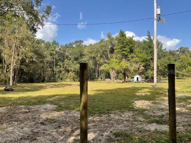 A grassy, wooded lot features two wooden fence posts in the foreground — 5542 SW 57TH AVENUE, GAINESVILLE, FL