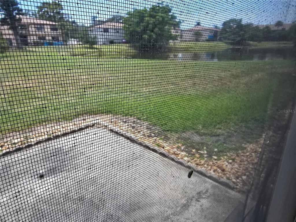 A view of a grassy yard and a pond through a screened-in patio door — 5064 LIVE OAK CIR UNIT 5064, BRADENTON, FL