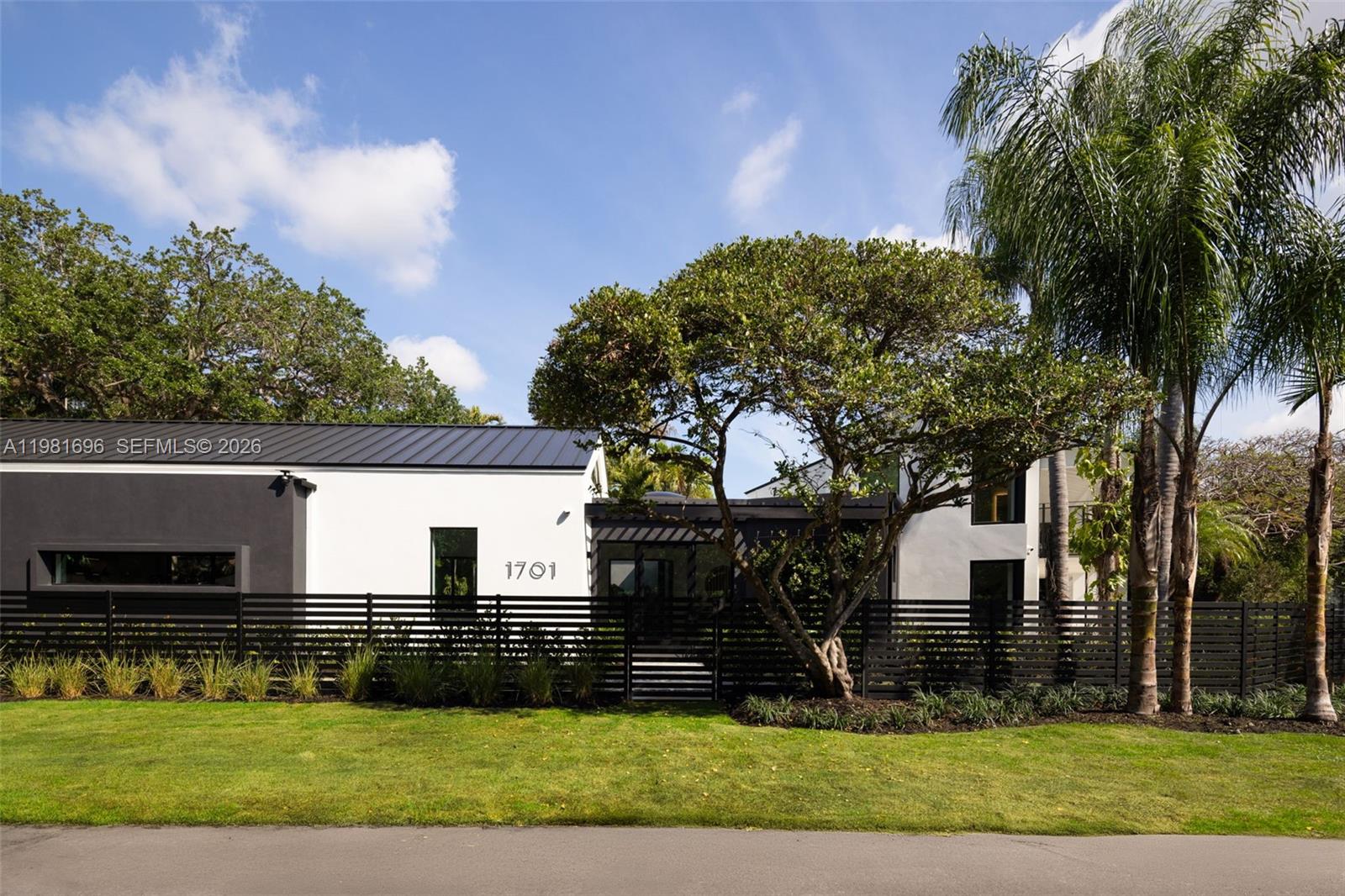 A modern white and black house features a horizontal slat fence and a large tree — 1701 Micanopy Ave, Coconut Grove FL 33133, COCONUT GROVE, FL