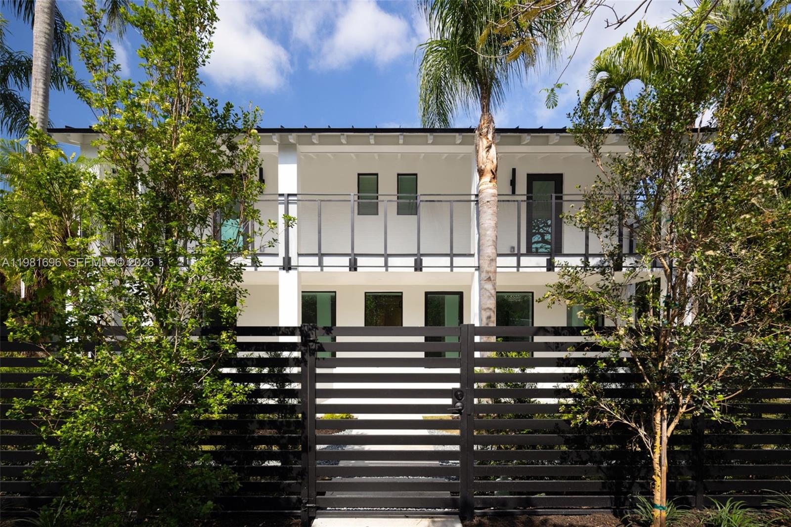 A two-story white house with a black horizontal slat fence and a second-floor balcony — 1701 Micanopy Ave, Coconut Grove FL 33133, COCONUT GROVE, FL