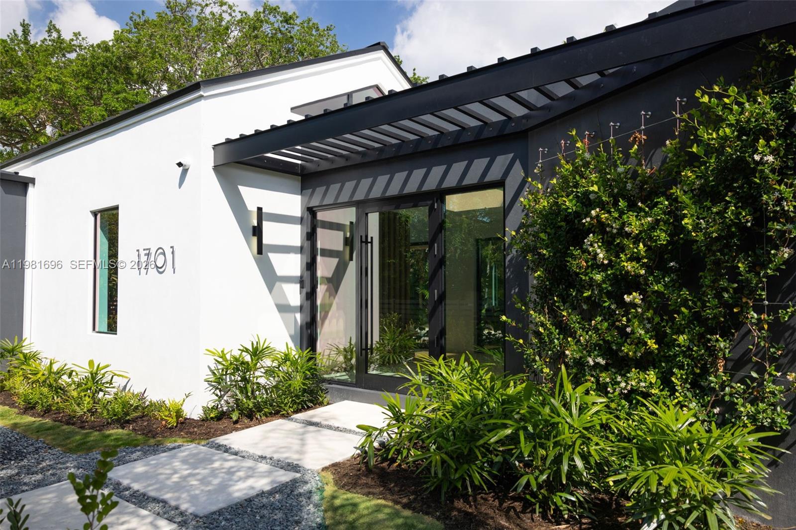 The exterior of a modern home features white and black walls with a pergola entrance — 1701 Micanopy Ave, Coconut Grove FL 33133, COCONUT GROVE, FL