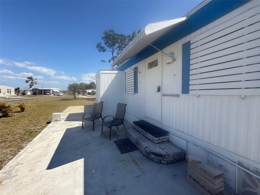 A mobile home exterior features a concrete patio, two chairs, and a set of steps — 7428 ARBELA STREET, PORT CHARLOTTE, FL