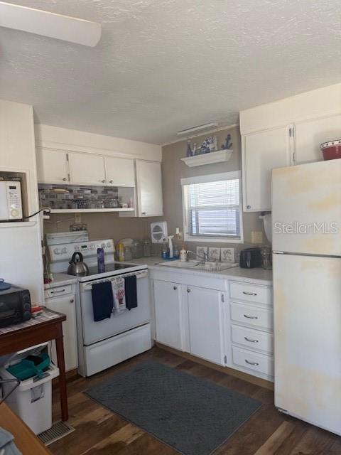 A kitchen features white cabinetry, a white stove, a refrigerator, and wood-look flooring — 7428 ARBELA STREET, PORT CHARLOTTE, FL