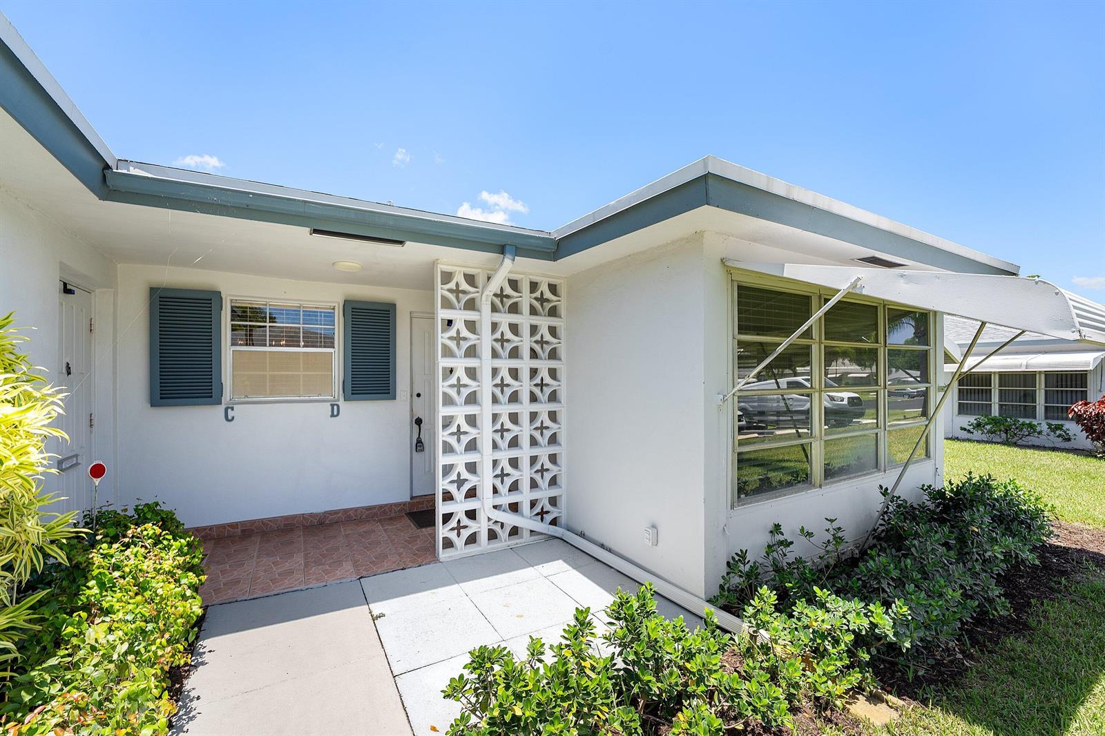 The exterior of a white house features a decorative breeze block screen and shutters — 1210 S Drive Circle # D, Delray Beach FL 33445, DELRAY BEACH, FL