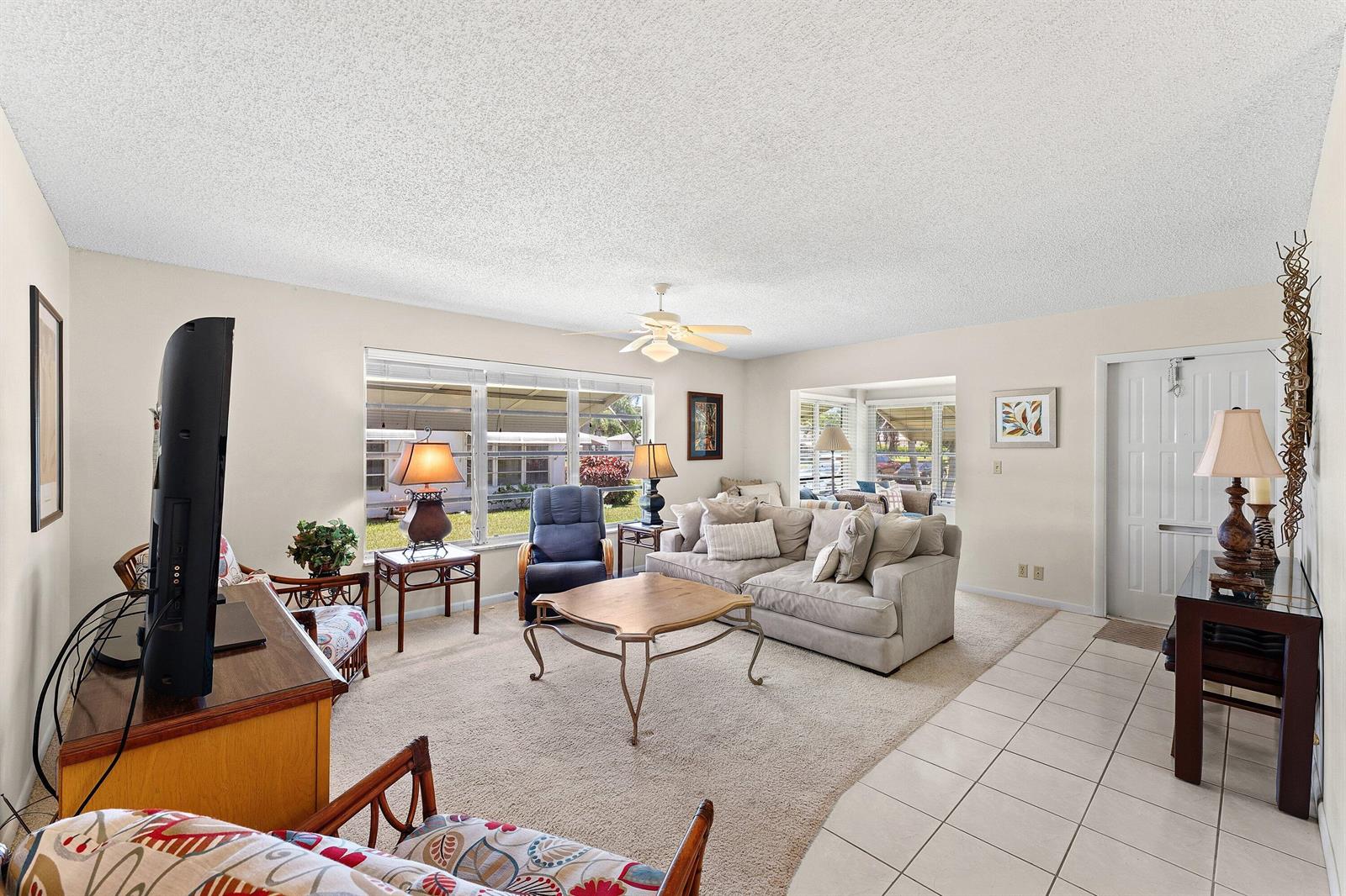 A living room features a beige sofa, a coffee table, and a large television — 1210 S Drive Circle # D, Delray Beach FL 33445, DELRAY BEACH, FL