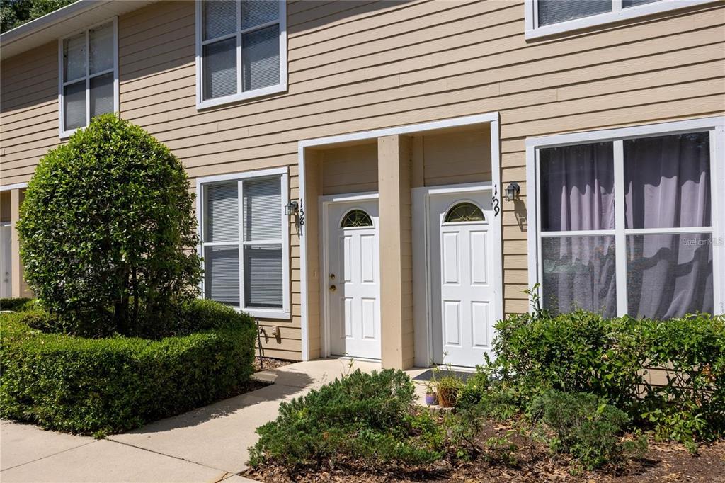 A two-story townhouse exterior with beige siding, two white front doors, and landscaped bushes — 3510 SW 30TH WAY UNIT 158, GAINESVILLE, FL