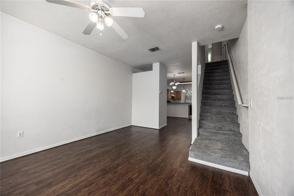 A living room with dark wood-look flooring, white walls, a ceiling fan, and carpeted stairs — 3510 SW 30TH WAY UNIT 158, GAINESVILLE, FL