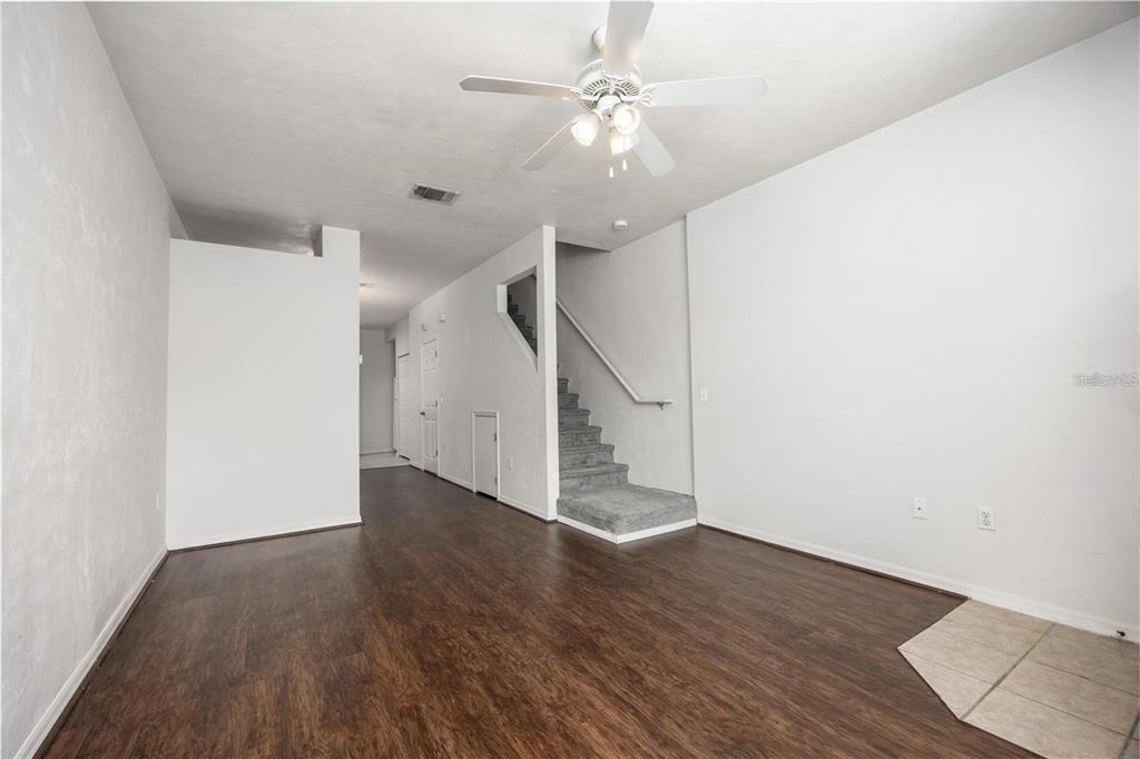 An empty living room features dark wood-look flooring, white walls, a ceiling fan, and stairs — 3510 SW 30TH WAY UNIT 158, GAINESVILLE, FL
