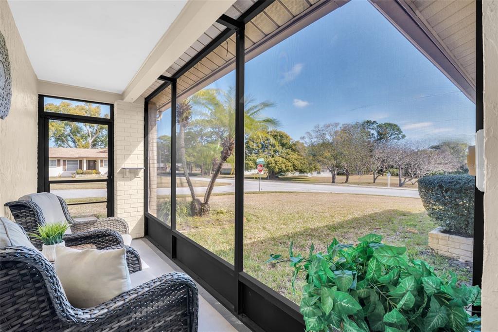 A screened-in porch features wicker chairs and a view of a suburban street and lawn — 102 STAFFORD DRIVE, PALM HARBOR, FL