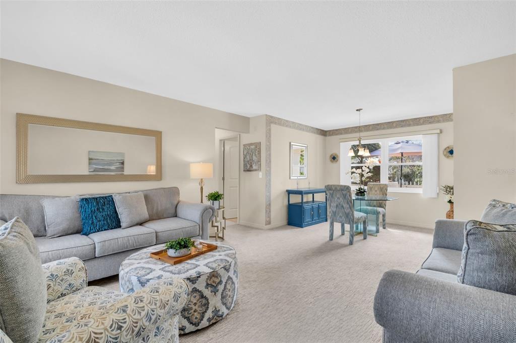 A living room and dining area with gray sofas, a patterned ottoman, and carpeted floors — 102 STAFFORD DRIVE, PALM HARBOR, FL