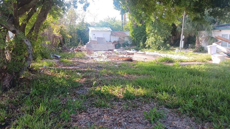 A vacant lot features overgrown grass, debris, and a small shed in the background — 6706 STOCK STREET, PORT RICHEY, FL