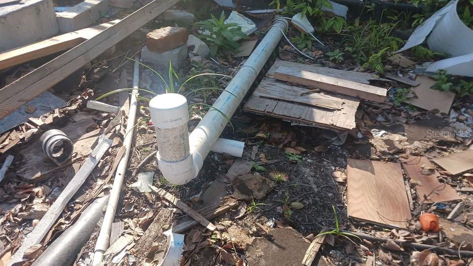 A white PVC pipe assembly lies on the ground amidst construction debris and scattered vegetation — 6706 STOCK STREET, PORT RICHEY, FL