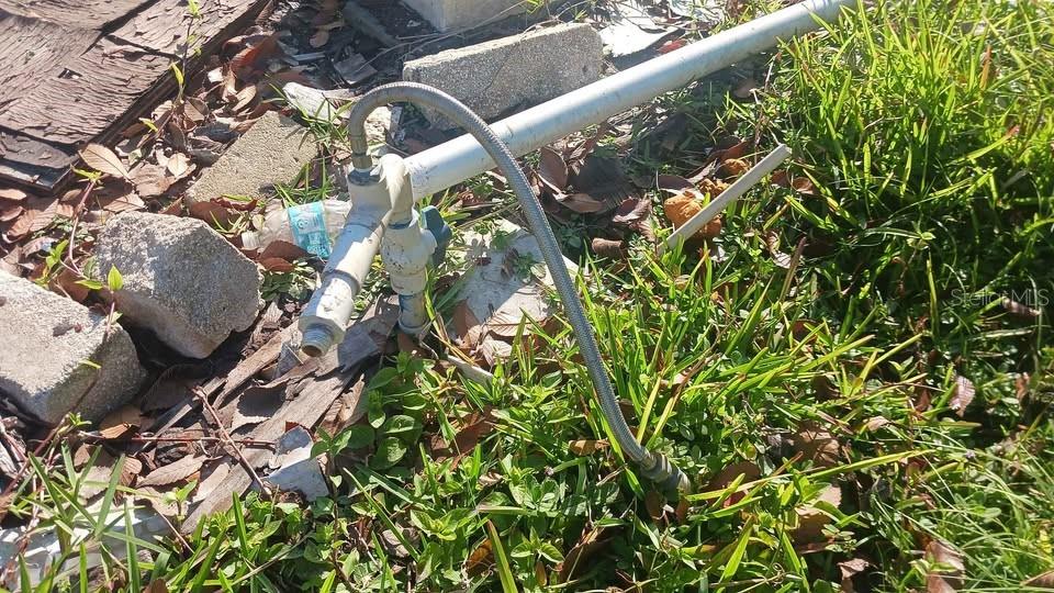 An outdoor metal pipe assembly with a flexible hose sits on the ground near grass — 6706 STOCK STREET, PORT RICHEY, FL