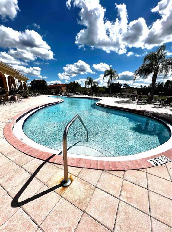 A curved swimming pool with a metal handrail sits on a tiled patio under clouds — 1820 CORIANDER DRIVE, POINCIANA, FL
