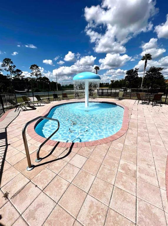A small outdoor swimming pool features a blue mushroom-shaped fountain under a cloudy sky — 1820 CORIANDER DRIVE, POINCIANA, FL