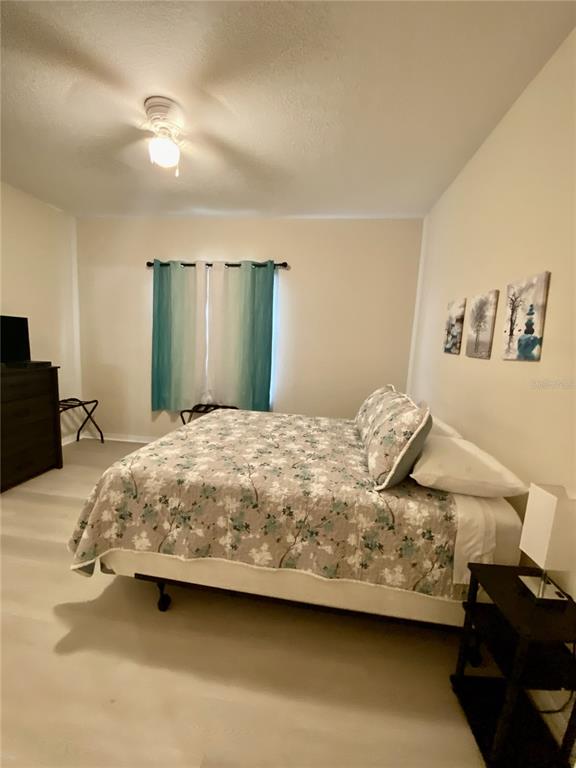 A bedroom features a bed with a floral quilt, teal curtains, and three wall-mounted pictures — 1820 CORIANDER DRIVE, POINCIANA, FL