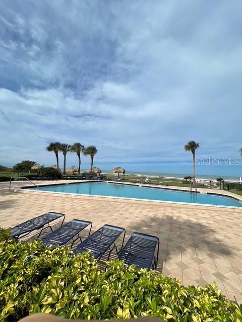 A swimming pool sits on a paved deck overlooking the ocean with palm trees nearby — 1460 GULF BOULEVARD UNIT 707, CLEARWATER BEACH, FL