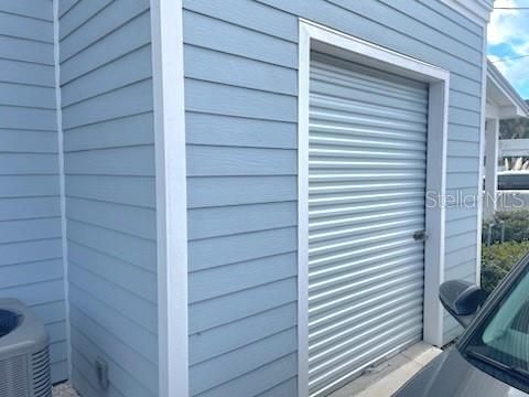 A light blue exterior wall features a metal roll-up storage door and an adjacent air conditioner — 308 W BRIDGERS AVENUE, AUBURNDALE, FL