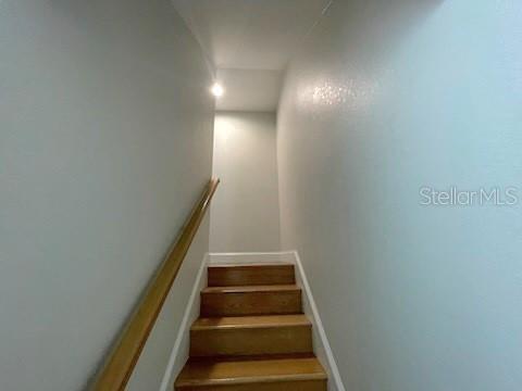 A staircase with wooden steps and a wooden handrail leads upward between two plain walls — 308 W BRIDGERS AVENUE, AUBURNDALE, FL