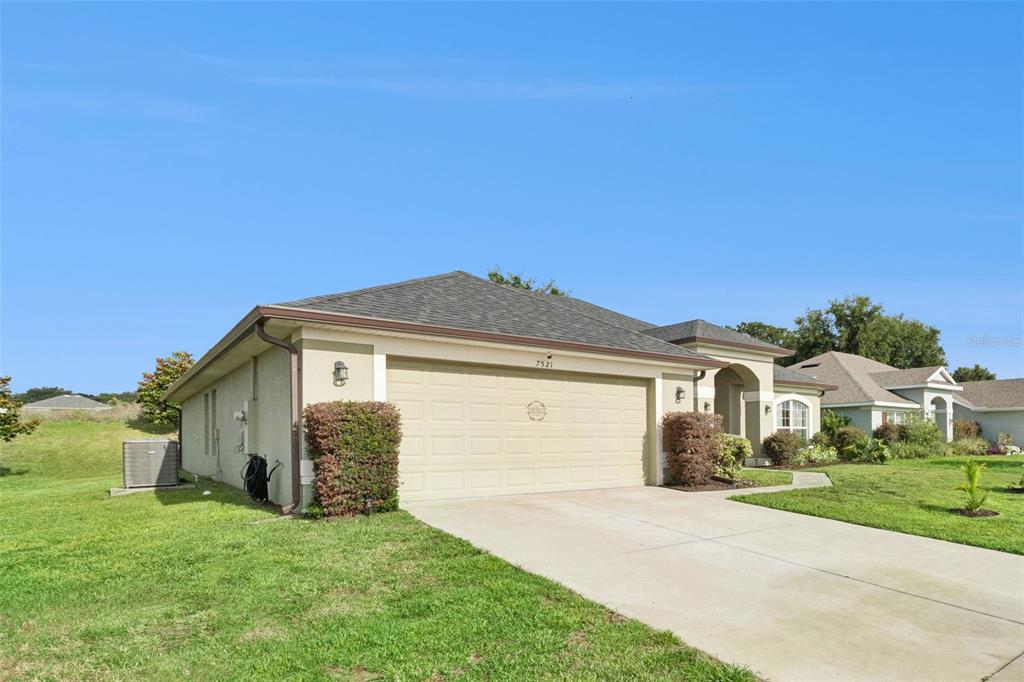 A single-story house with a beige stucco exterior, a two-car garage, and a shingled roof — 7521 SLOEWOOD DRIVE, LEESBURG, FL