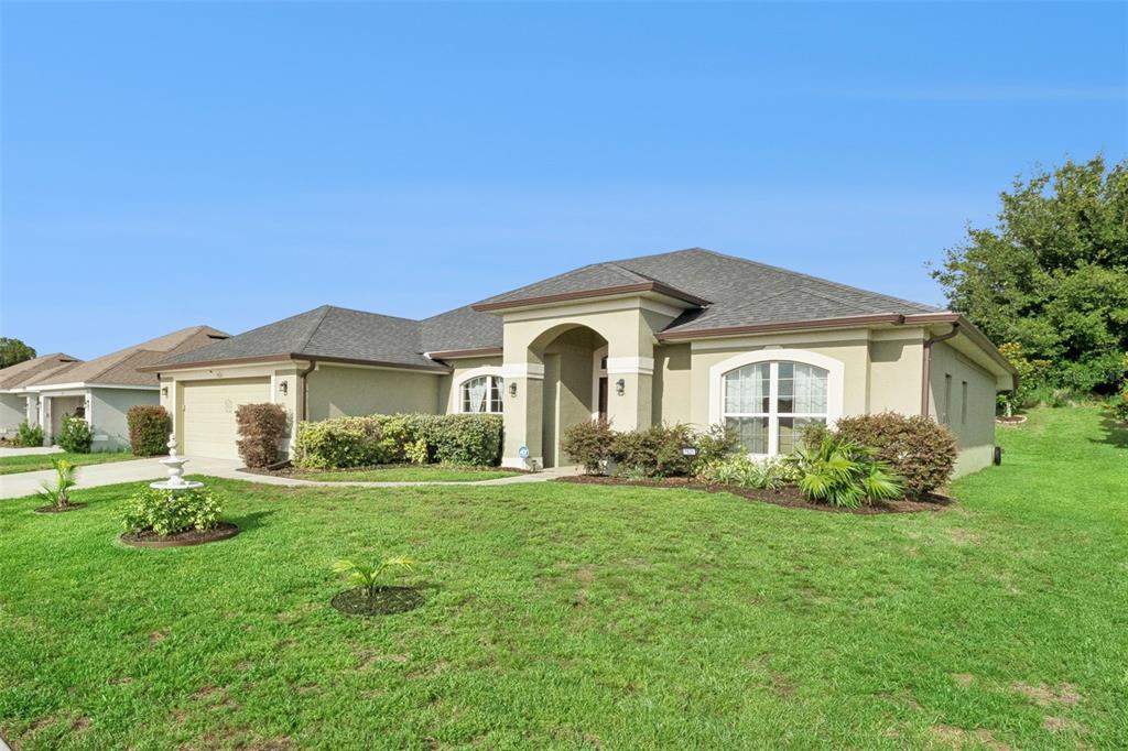 A single-story suburban house with a tan stucco exterior, arched entryway, and a grassy lawn — 7521 SLOEWOOD DRIVE, LEESBURG, FL