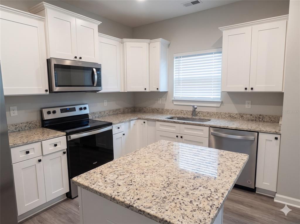 A kitchen features white cabinets, granite countertops, stainless steel appliances, and a central island — 3044 N 7TH AVENUE, MILTON, FL