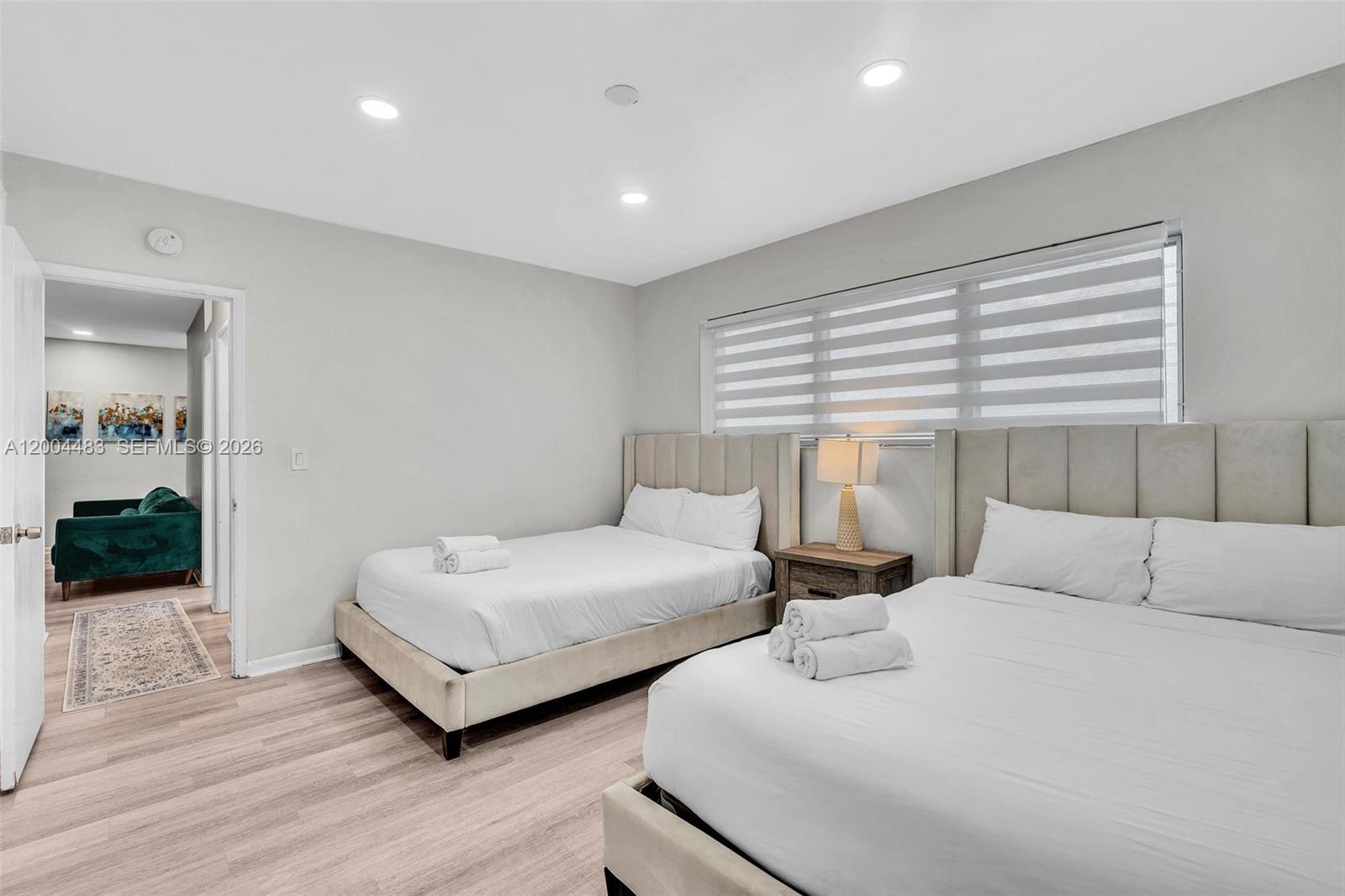 A bedroom features two beds with light-colored headboards, wood-look flooring, and a window with blinds — 10006 E Bay Harbor Dr # 17, Bay Harbor Islands FL 33154, BAY HARBOR ISLANDS, FL