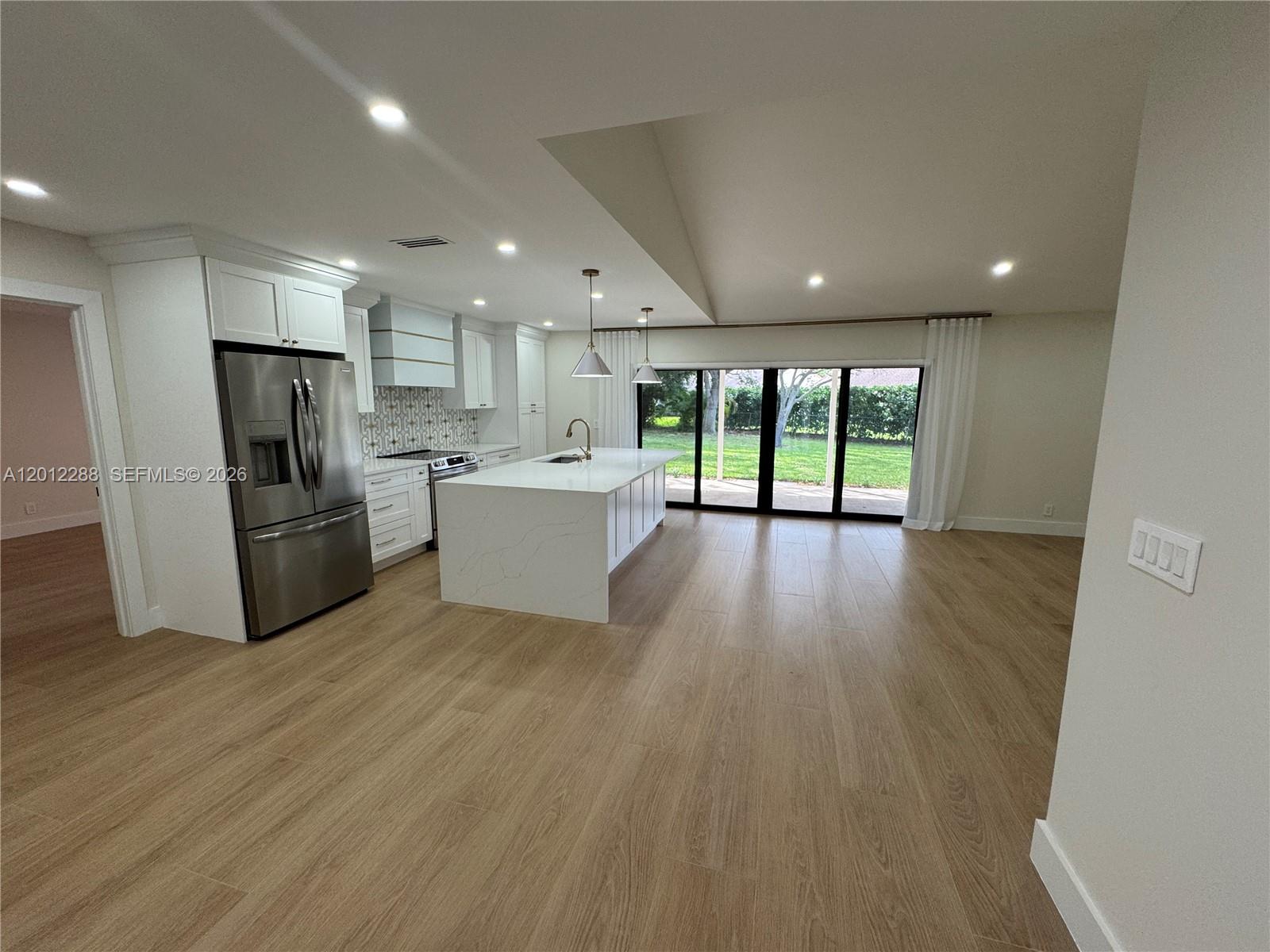 A modern kitchen features white cabinetry, a marble-topped island, and sliding glass doors to a yard — 9234 Southampton Pl, Boca Raton FL 33434, BOCA RATON, FL