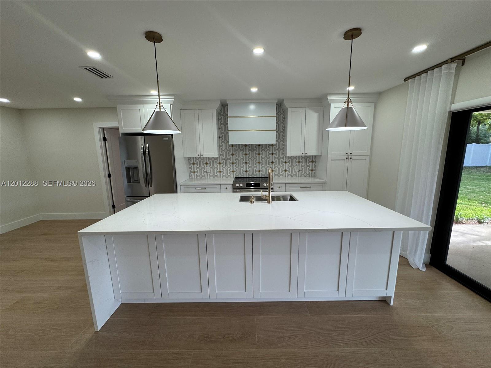 A modern kitchen features a large white quartz island, white cabinetry, and a patterned backsplash — 9234 Southampton Pl, Boca Raton FL 33434, BOCA RATON, FL